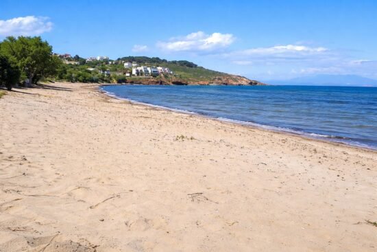 Wide sandy beach at Karfas in Chios with calm Aegean Sea and hillside houses in the background